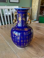 Photo of blue ceramic Chinese vase with gold lettering and double gold handles, showing front details.