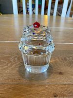 Front view of clear crystal cupcake figurine with faceted frosting and embedded multicolored stones, topped with red crystal cherry.