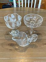 Group photo of two clear crystal footed bowls and one swan-shaped dish on wooden table.