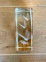 Clear rectangular crystal with three butterflies and a flower etched inside, photographed on wooden surface