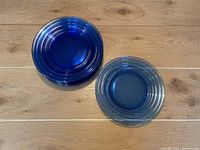 Photo showing stacks of blue glass plates with circular ridge pattern on a wooden surface.