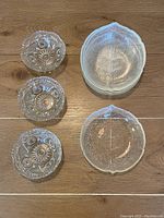 Three small cut crystal bowls and two clear glass leaf-shaped plates on wooden floor.