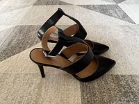 Side angled view of one black ladies dress shoe showing two broad straps and pointed toe on beige patterned carpet.