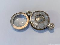 Open swivel-out magnifying glass revealing the lens within the silver frame along with mother of pearl decorated top.