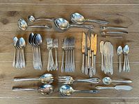 Full layout of all silverware pieces arranged on wood surface showing 6 place settings plus serving utensils.
