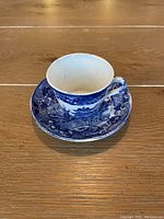 Small blue and white porcelain teacup on matching saucer with Japanese motif, set on wooden surface.