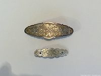 Two sterling silver hair clips with engraved floral designs placed on a white surface. The larger clip is at the top and the smaller below it.