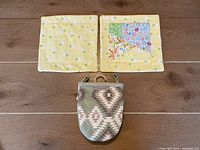 Two yellow 8x8 inch pot holders laid flat, one with patchwork and animal/umbrella prints, the other mostly yellow with bunny print; unopened oven finger mitt in front with tan and brown geometric pattern.
