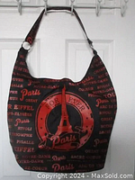 Front view of black canvas tote hobo bag with red Paris-themed surface print showing text and Eiffel Tower emblem and single shoulder strap.