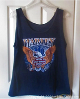 Front view of black Harley Davidson tank top hanging on a hanger showing eagle design and the word Harley on top.