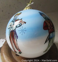 Side view showing painted characters on glass ornament including a violin player and other figures frolicking in the snow on a blue and white background.