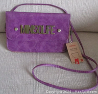 Front view of purple faux leather Miniso mini crossbody bag with brass Minisolife logo on flap, removable strap, and tag attached.