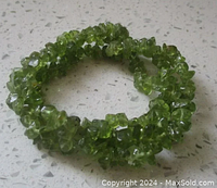 Photo showing the full stretch bracelet with light green irregular peridot chips strung together, coiled on a flat surface