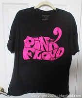Full view of the black Pink Floyd T-shirt with large bright pink retro logo on the front, hanging on a hanger.