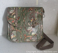 Front view of Sakroots Artist Circle bag showing olive green color with owl and floral accents, snap flap, and brown canvas strap.