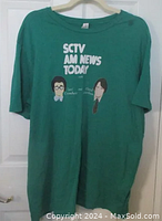 Full view of green t-shirt hanging on a hanger showing front graphics and text.