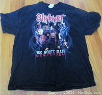 Full view of black Slipknot We Won't Die Tour t-shirt front on wooden floor.