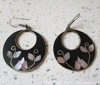 Pair of round black enamel earrings with abalone shell floral accents and hook closures, photographed on a white speckled surface.