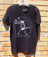 Full view of black short-sleeve t-shirt hung on a clear plastic hanger showing the Vitruvian Man with electric guitar print on the front.