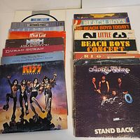 Photo of stacked classic vinyl LP records showing album artwork including Kiss Destroyer and The Moody Blues, and other records from Meat Loaf, Duran Duran, The Beach Boys, Prism, and more.