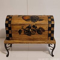 Front view of wooden chest with painted fruit design and black checkerboard accents, metal latch, and steel legs.