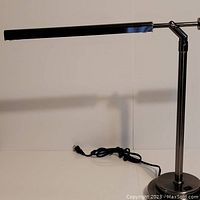 Full view of the pewter colored desk lamp with a long rectangular lamp head and power cord visible.