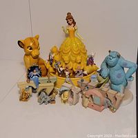 Full view of assorted Disney collectible figurines including Belle in yellow dress, Simba, Sulley, Pooh figures with numbers, and small animal figures