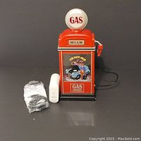 Front view of red gas pump decoration with colorful vintage car cartoon motif and accessories laid in front.