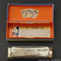 Top view of open box showing interior label and harmonica inside, metal cover having patina and wear.