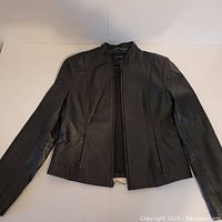 Black leather jacket laid flat on white surface showing front view with zipper closed halfway.