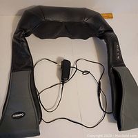 Full view of the U-shaped neck and shoulder massager with power cord and adapter visible