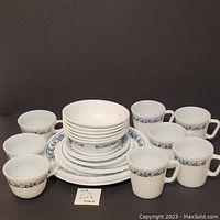 Photo of Corelle dinnerware stack with Pyrex coffee mugs and teacups around, all white with blue floral border.