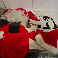 Full display of Santa costume items spread out, showing red pants, jacket, hats, wig, beard, belt, gloves, bell, and glasses