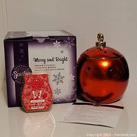 Red ceramic Scentsy warmer seen next to its purple and white holiday-themed box labeled 'Merry and Bright,' along with sealed red wax bars labeled 'Coastal Strawberry' in front.