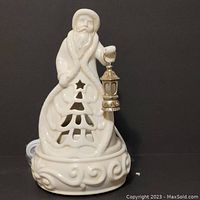 Close-up front view of white ceramic Scentsy warmer shaped as Old World Santa holding a lantern with ornamental cutout details on base.