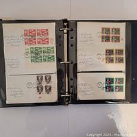 Open binder showing pages with postmark stamps in blocks affixed to black pages, each block of stamps cancelled with postmarks and with handwritten annotations.