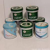 Set of 8 vintage metal tobacco and cigarette tins with three Player's Light tins and five Export tins arranged in staggered formation.