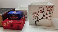 Two square white ceramic vases with red cherry blossom branch designs, two red decorative boxes, one larger and one smaller, placed together on a flat surface.