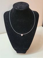 Single delicate necklace with small heart-shaped clear crystal pendant on thin silver chain displayed on black bust stand.