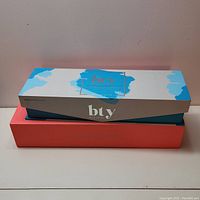 Two stacked boxes: Top is turquoise and white BTY box; bottom is coral color with 'Straight Up Perfection' text.