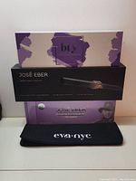 Three boxed hair styling items stacked showing the Btx ionic heat brush box on top, José Eber clipless curling iron box in the middle, and Eva NYC heat mat pouch on bottom.