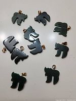 Photo of 10 dark green jade animal-shaped pendants arranged on a white background, showing smooth carved jade pieces with gold-tone bails attached at the top.