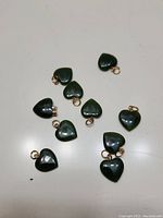 10 dark green jade heart-shaped pendants with gold-colored loops spread on a white surface.