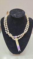 Full view of the Kimono pearl necklace displayed on a black necklace bust showing the pearl strand and attached tag.