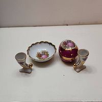 Porcelain set including a small bowl, egg-shaped trinket box, and two candle holders arranged on white surface.