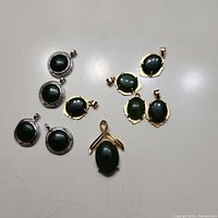 Top view of all 10 jade pendants arranged on a table showing gold and silver frames and ribbon style design pendant.