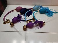 Photo showing six vintage-style perfume atomizer tops with various colors of mesh-covered bulbs, tassels, gold-tone caps, and spray tubes, displayed on a white surface.