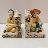 Front view of two porcelain Asian figurine bookends showing detailed seated figures on marbled bases