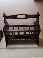 Front view of a dark wood magazine rack showing handle cutout and slat details
