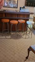Full view of four vintage bar stools showing three brown seats and one white seat, placed in front of a wooden bar counter.